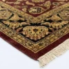 Detailed corner view of a crimson Indian rug showing the ornate black botanical border and clean white hand-bound fringe.