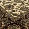 Detailed corner view of an ivory Indian rug showing the ornate dark brown botanical border and clean white hand-bound fringe.