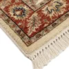 Detailed corner view of an ivory Indian wool rug showing the ornate terracotta botanical border and clean white hand-bound fringe.