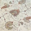Macro shot of the hand-spun wool pile on an ivory Indian rug, showing soft natural color variations in the terracotta and sage green floral motifs.