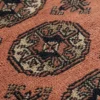 Macro shot of the dense hand-knotted wool pile on a coral Bokhara rug, showing a detailed octagonal gul motif and silky fiber texture.
