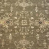 Macro shot of the hand-spun wool pile on an olive Chobi rug showing muted cream floral motifs and natural abrash color variations.
