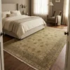 Bright modern bedroom with a neutral bed and light wood floors, featuring a 6' x 9' muted sage and gold Chobi wool rug.