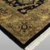 Detailed corner view of a black Indian rug showing the ornate golden-tan botanical border and clean white hand-bound fringe.