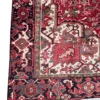 Detailed corner view of a red Persian Heriz rug showing the ornate botanical border, dark navy spandrels, and secure hand-bound edges.