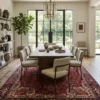 Modern formal dining room with a long walnut table and neutral chairs, anchored by a large red Persian Heriz rug under a brass chandelier.