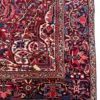 Close-up corner view of a red Persian Heriz rug showing the multi-layered botanical border and secure hand-knotted edge finish.