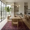 Modern formal dining room with a long light-oak table and minimalist chairs, featuring a large Heriz rug providing a prestigious anchor.