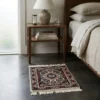 Serene bedroom with dark concrete floors and a walnut nightstand, featuring a small hand-knotted Indian wool rug placed beside the bed.