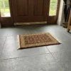 Luminous modern entryway with a walnut front door and large gray floor tiles, featuring a small burgundy Indian wool accent rug centered in front of the door.