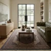 Luminous modern living room with a green tufted leather sofa and oak coffee table, anchored by a traditional charcoal Indian wool area rug.