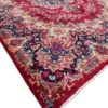 An angled perspective view of a large red and navy Iran Darbari rug, showcasing the intricate floral patterns and the substantial, luminous wool pile.