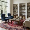 Bright sitting area with built-in bookshelves and blue wingback chairs, anchored by a large red Iran Darbari rug providing a warm foundation.