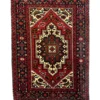 Overhead view of a 1' 10" x 2' 6" hand-knotted Iranian Gholtogh wool rug featuring a vibrant blue hexagonal medallion on a saturated red field.