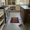 Luxurious modern kitchen with white cabinetry and a farmhouse sink, featuring a small blue and red Gholtogh rug as a vibrant accent on a polished concrete floor.