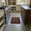 Luxurious modern kitchen with a stainless steel range and walnut cabinetry, featuring a small red Gholtogh Persian rug as a vibrant accent on gray concrete floors.
