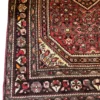 Technical corner view of a Persian Hosinabad rug highlighting the thick charcoal floral border, cream corner framing, and hand-bound edges.