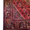 Detailed corner view of a red Persian Joshaghan rug showing the intricate navy botanical border, geometric corner layout, and secure edge finish.