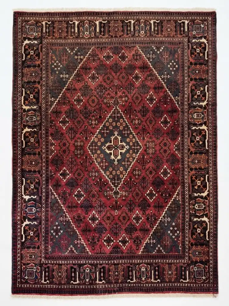 Full overhead view of a 7' 0" x 10' 0" hand-knotted Iranian Joshaghan wool rug with an intricate geometric diamond medallion on a saturated red and navy field.