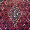 Macro shot of the dense hand-knotted wool pile on an Iranian Joshaghan rug, showing intricate repeating geometric flower and leaf motifs.