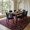 Minimalist modern dining room with a long wooden dining table and sleek contemporary chairs, centered over a red and navy Persian Joshaghan wool rug.