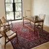 Modern home office with built-in bookshelves and a minimalist desk, anchored by a 7x10 red and navy Persian Joshaghan wool rug on concrete floors.