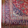 Close-up corner view of a Persian Kashan rug highlighting the dense indigo floral border, ivory guard lines, and flat hand-bound edge finish.