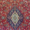 Macro shot of the dense hand-knotted wool pile on an Iranian Kashan rug, highlighting the fine curvilinear floral patterns and rich red and navy colors.