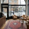 High-end modern coffee shop with walnut bar counters and bistros, anchored by a large red Kashan Persian rug under wood and leather seating.