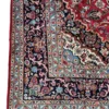 Detailed corner view of a red Persian Kashan rug showing the ornate navy botanical border and secure hand-knotted edge finish.