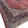 An angled perspective view of a large red and navy Persian Kashan rug, showcasing the intricate border patterns and the substantial, luminous wool pile.