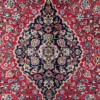 Macro shot of the dense hand-knotted wool pile on a Kashan rug showing the central medallion with intricate navy, ivory, and light blue floral details.