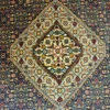 Close-up macro shot of the high-density hand-knotted wool pile on an Iranian Mahi rug, showing the intricate blue, orange, and amber yellow repeating leaf and fish motifs.
