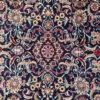 Macro shot of the dense hand-knotted wool pile on a Mood rug showing intricate gold, red, and ivory floral motifs on a navy background.