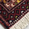 Detailed corner view of a green and red Iranian wool rug showing the intricate geometric border and secure hand-knotted edge finish.