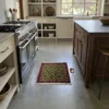 Luxurious modern kitchen with a stainless steel range and walnut cabinetry, featuring a small green Persian rug as a vibrant accent on a polished concrete floor.