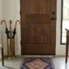 A luminous modern entryway with a walnut and glass front door and polished concrete floors, featuring a small navy and orange Qashqai tribal rug as a welcoming accent.