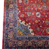 Close-up corner view of a Persian Sarough rug highlighting the dense indigo floral border, vibrant red field, and hand-bound edge finish.