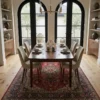Sophisticated dining room featuring a long wooden table and beige upholstered chairs, centered over an intricate 7x10 Tabriz area rug under arched windows.