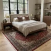Peaceful primary bedroom with a mid-century walnut bed frame and beige linens, anchored by an intricate red Tabriz Persian rug under a massive arched window.