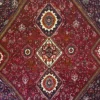 Macro shot of the dense hand-knotted wool pile showing intricate geometric configurations in ivory, gold, and terracotta against a crimson field.