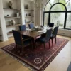 Elegant open-concept dining room featuring a long wooden dining table and navy upholstered chairs, centered over a 6x10 red and plum Persian rug.