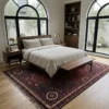 Bright minimalist bedroom with a walnut bed frame and large arched windows, anchored by a deep red and plum Iranian wool area rug.