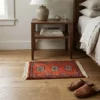 Serene bedroom with oak floors and a walnut nightstand, featuring a small rust-red Bokhara wool rug placed beside the bed.