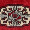 Macro shot of the dense hand-knotted wool pile on a red Bokhara rug showing the intricate geometric ivory gul motif and soft texture.