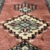 Macro shot of the dense hand-knotted wool pile on a rose Jaldar rug showing the intricate geometric diamond motif and high-luster texture.