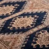 Macro shot of the dense hand-knotted wool pile on a navy Jaldar rug showing the intricate geometric diamond motif and high-luster texture.