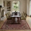 Traditional Iranian Hoseinabad wool rug under a rustic wooden dining table with green velvet chairs and a crystal chandelier.