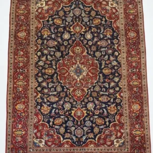 Full overhead view of a 6' 6" x 9' 10" hand-knotted Iranian Kashan wool rug featuring an ornate central medallion on a midnight navy field with red floral borders.