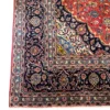 Detailed corner view of a red and navy Persian Kashan rug highlighting the multi-guard botanical border, ivory framing, and neat fringe lines.